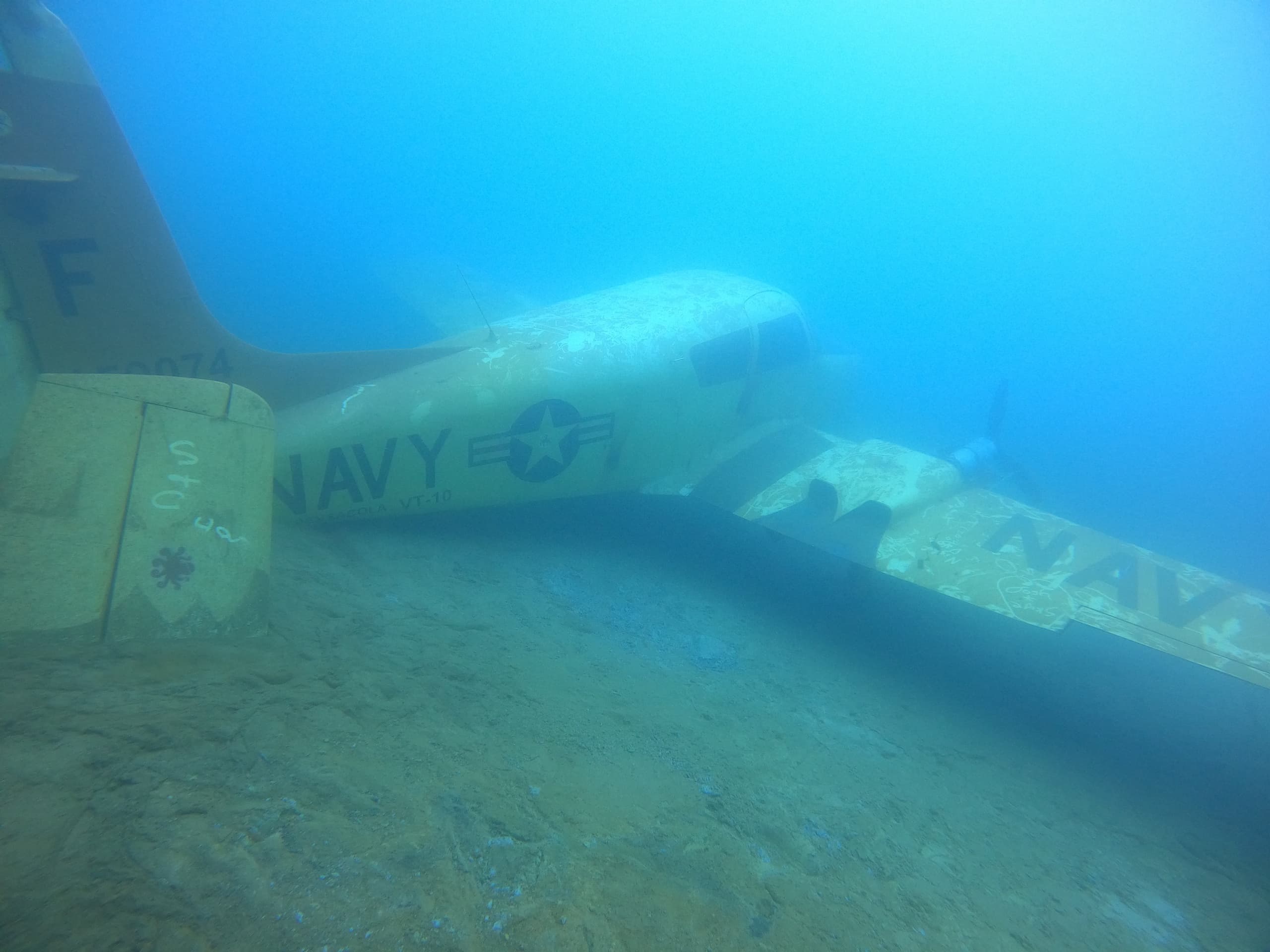 Scuba divers exploring submerged navy plane wreck on sandy bottom