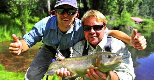 Anglers holding large trout on riverbank during fly fishing