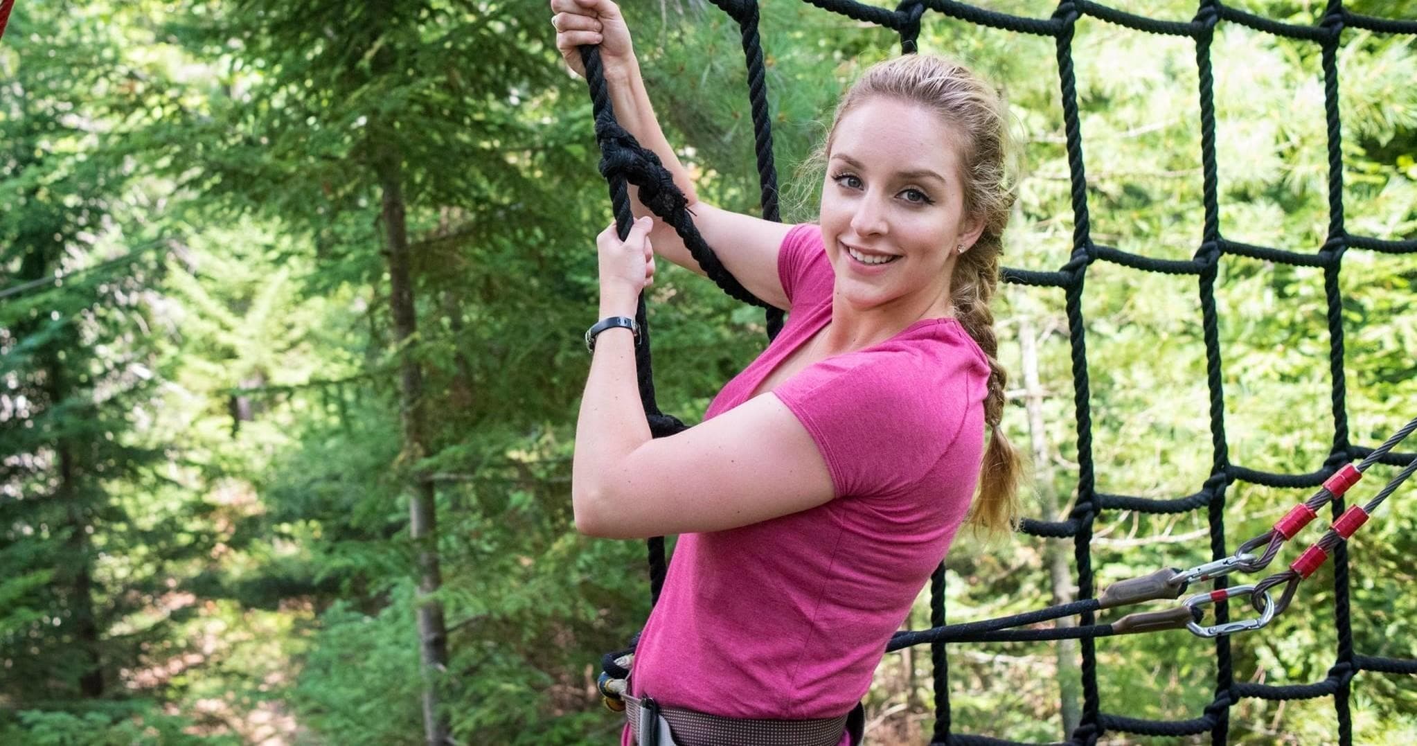 Smiling woman on treetop rope net course in evergreen forest