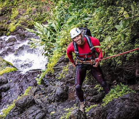 Adventurer ascending rocky jungle slope during canyoning trip
