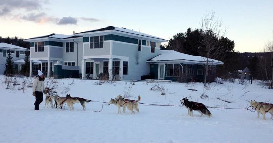 Dog sled team running past a snowy lodge in winter