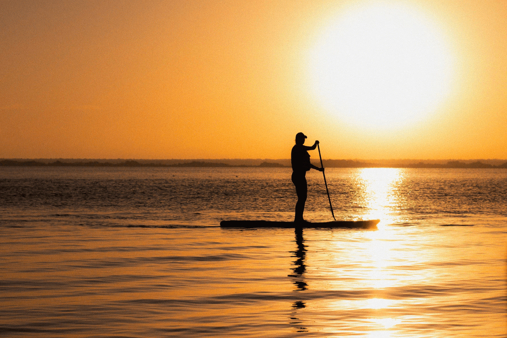 Solo stand-up paddleboarding silhouette on calm ocean sunset