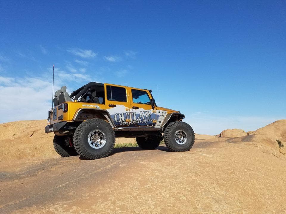 Yellow off-road Jeep on sandstone slickrock under blue sky