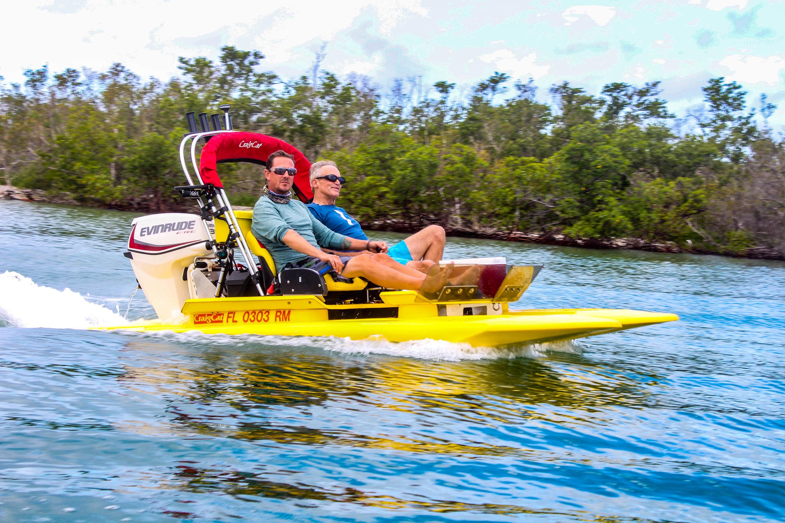 Couple riding yellow airboat fast through coastal mangrove waters