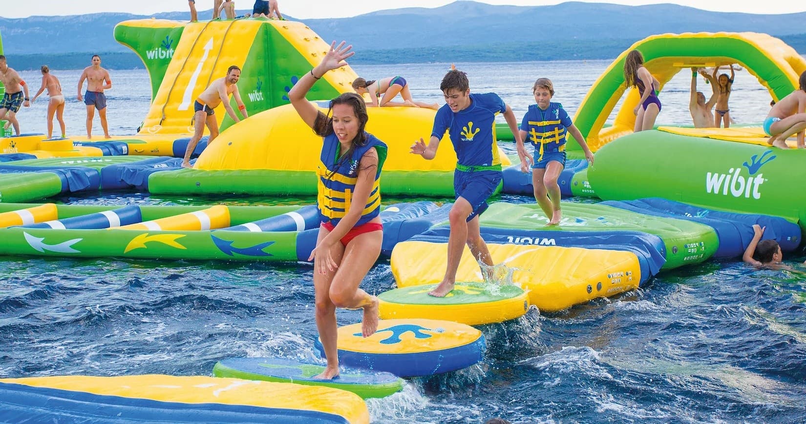 Adventurers on coastal inflatable waterpark navigating ocean obstacles