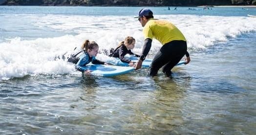 Surf instructor helping children stand on board in Whangamata surf