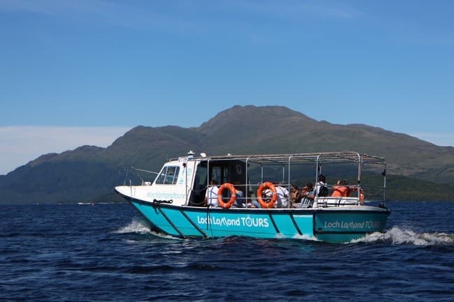 Tour boat cruising Loch Lomond with mountain backdrop, passengers