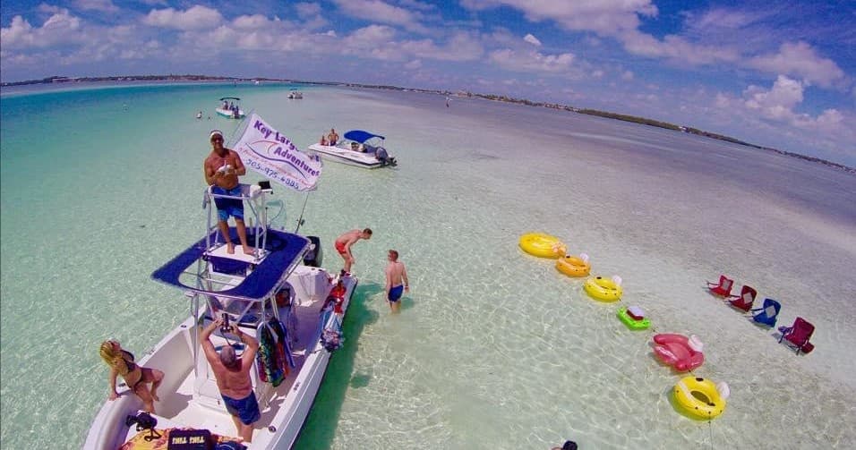 Aerial party boats anchored at crystal-clear sandbar beach