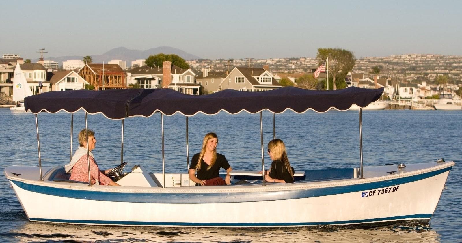 Covered sightseeing launch cruising calm harbor with city skyline