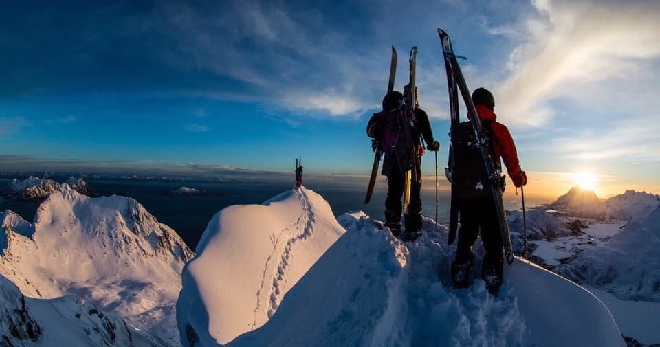 Skiers standing on snowy alpine ridge at sunrise, panoramic