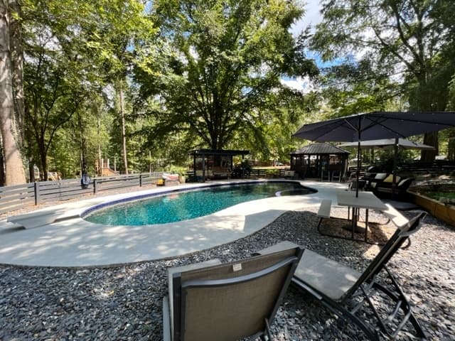 Outdoor pool and lounge area surrounded by shady trees
