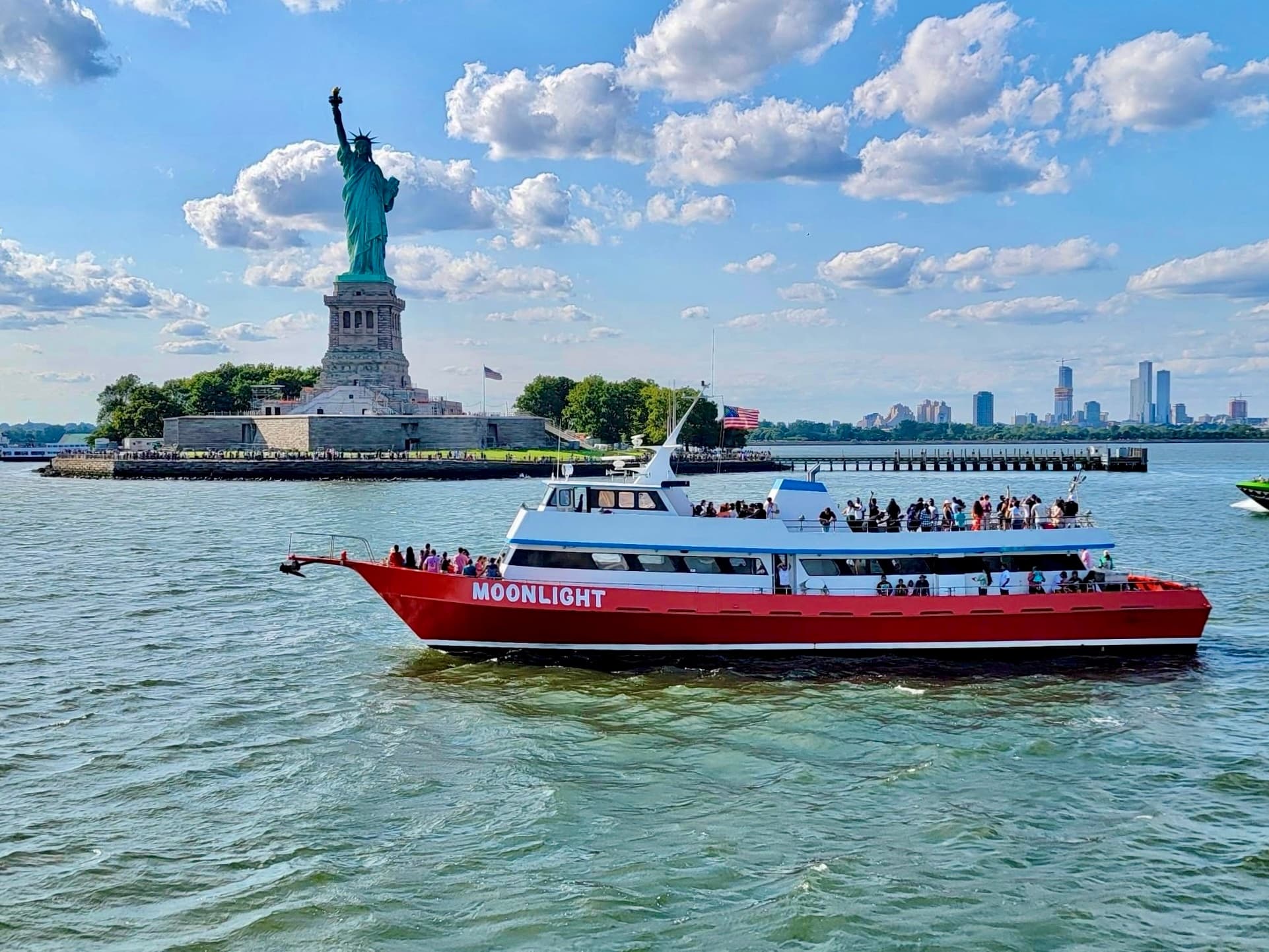 Red Moonlight cruise ferry by Statue of Liberty on clear day