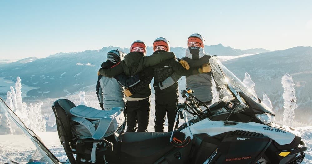 Group of snowmobilers posing on mountain ridge with panoramas