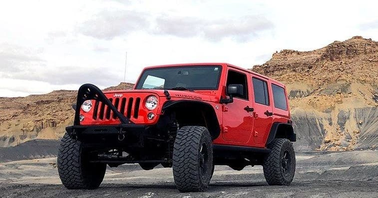 Red Jeep Wrangler off-roading on desert plateau with rocky buttes