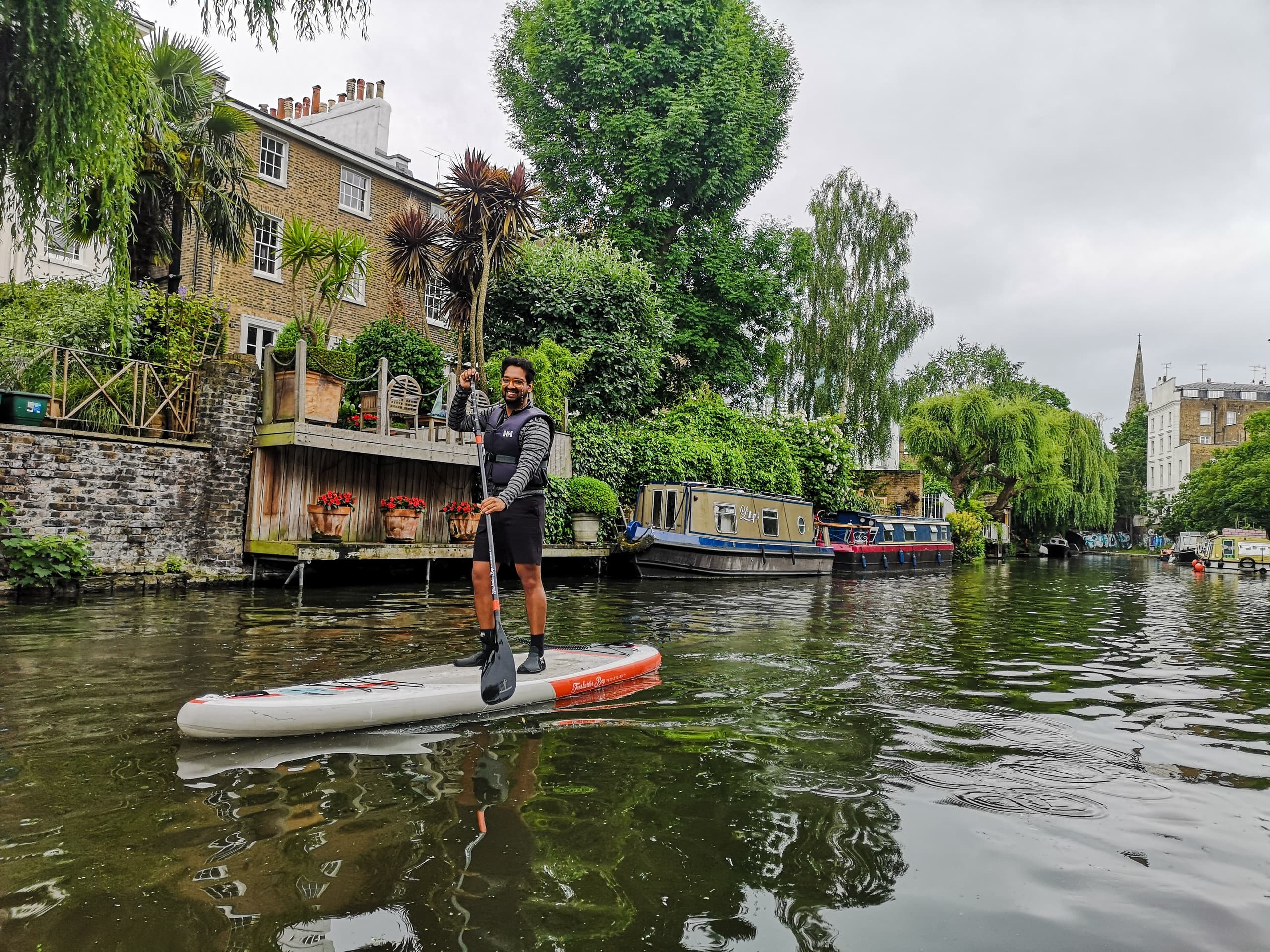 Solo paddleboarder cruising quiet canal past riverside houses