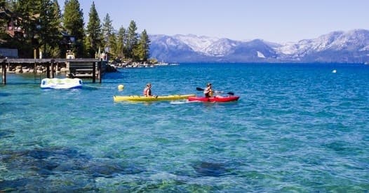 Kayakers near shoreline on clear turquoise lake with docks