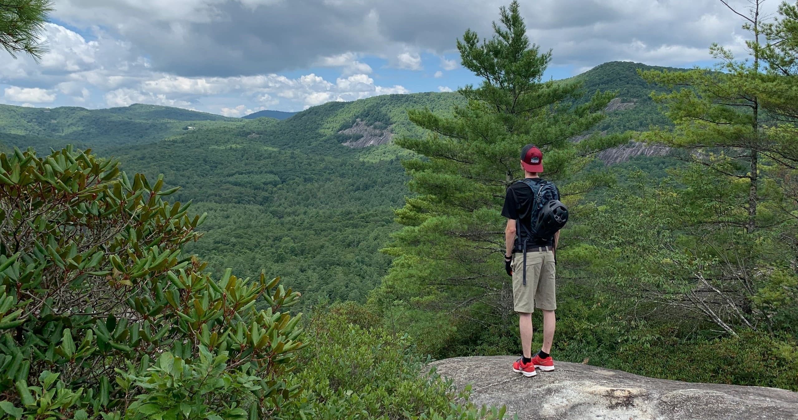 Hiker standing on rocky overlook above forested mountain ridge