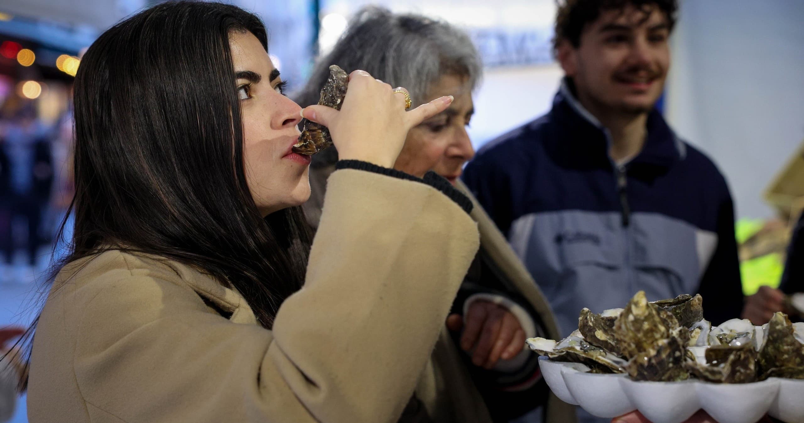 Woman tasting fresh oysters at lively French outdoor market
