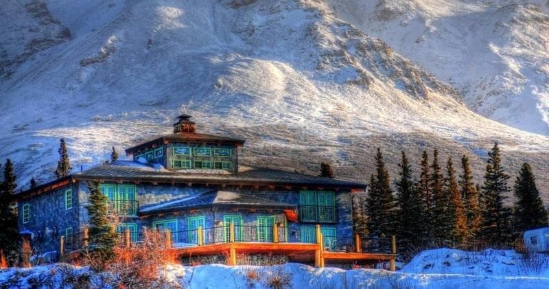 Snow-covered mountain lodge exterior with dramatic alpine view