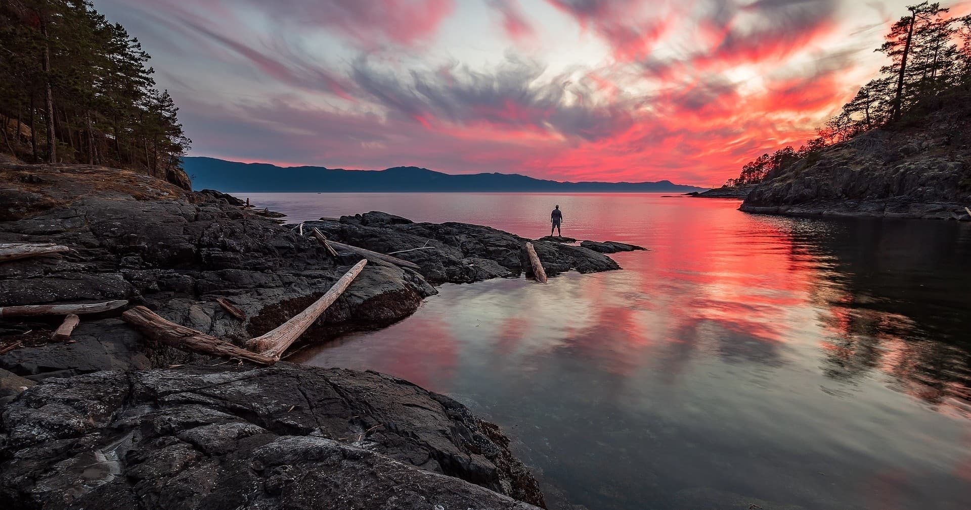 Person standing on rocky coastline at sunset, coastal view