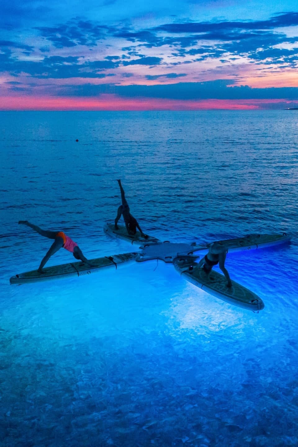 Kayakers paddling at dusk over glowing blue ocean lagoon