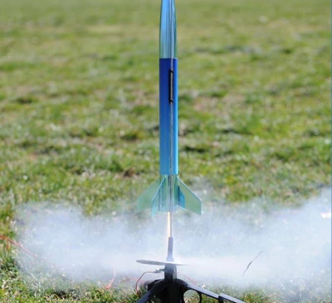 Model rocket launching from grassy field with smoke trail outdoors