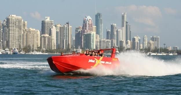 Red jet boat skimming coastal waters with city skyline backdrop