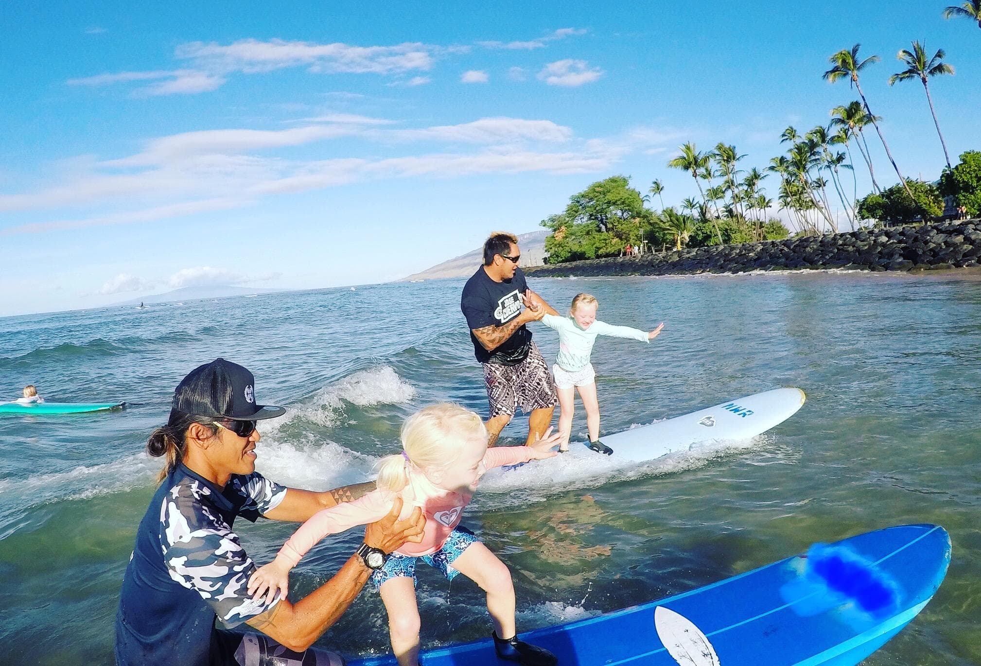 Family surf lesson on paddleboards near palm-lined Maui shoreline