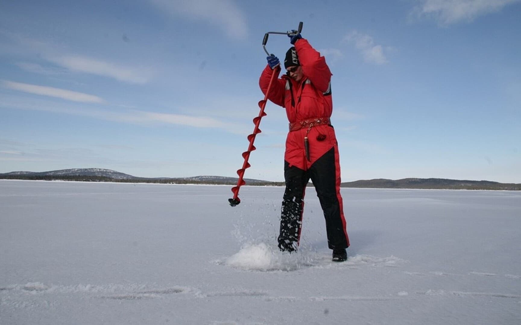 Ice angler drilling hole on frozen lake, winter ice fishing activity