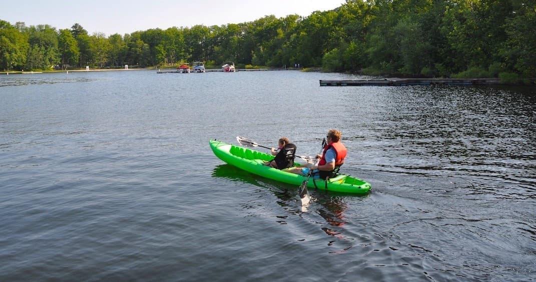 Two kayakers touring calm Lake Wallenpaupack near wooded shoreline