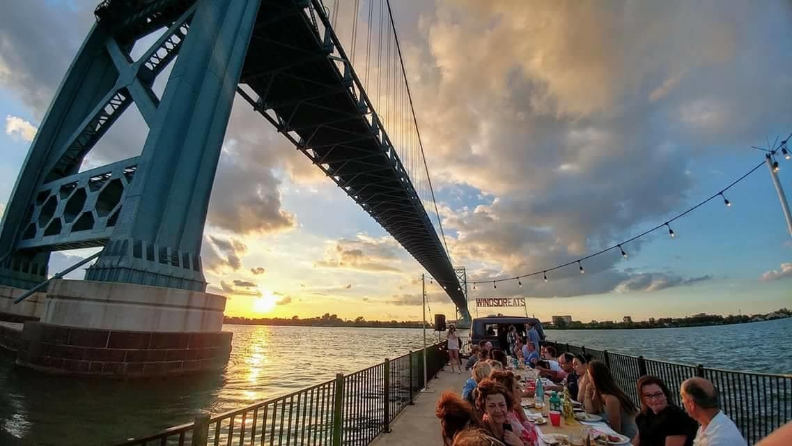 Sunset riverside dining under bridge with city skyline view