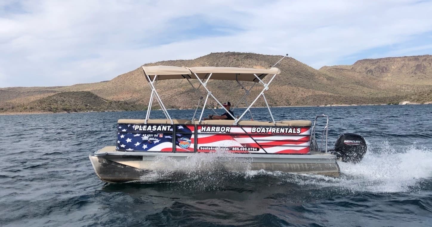 American-flag pontoon skimming lake with scenic hills backdrop