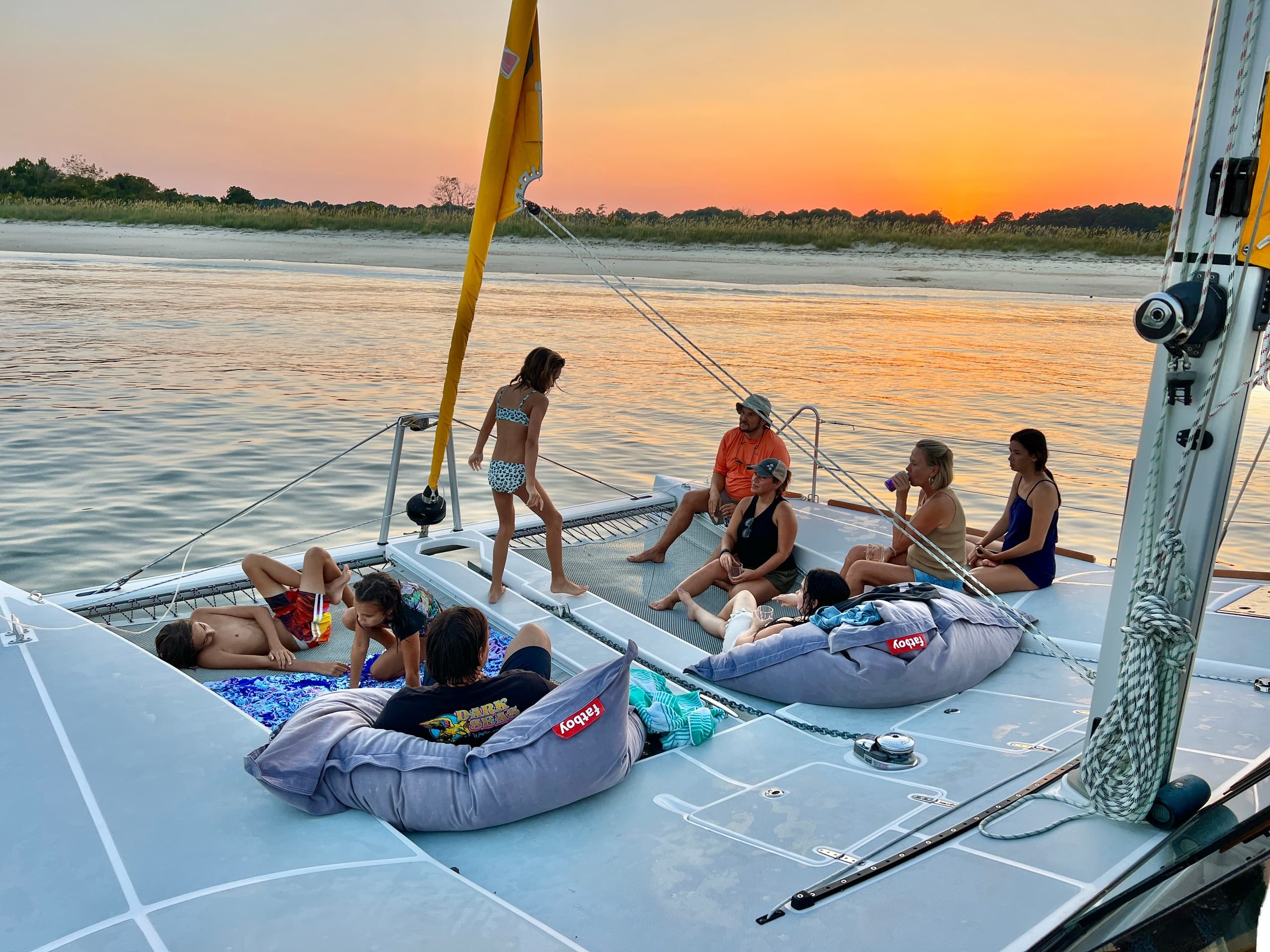 Friends relaxing on catamaran deck at sunset on coastal waters