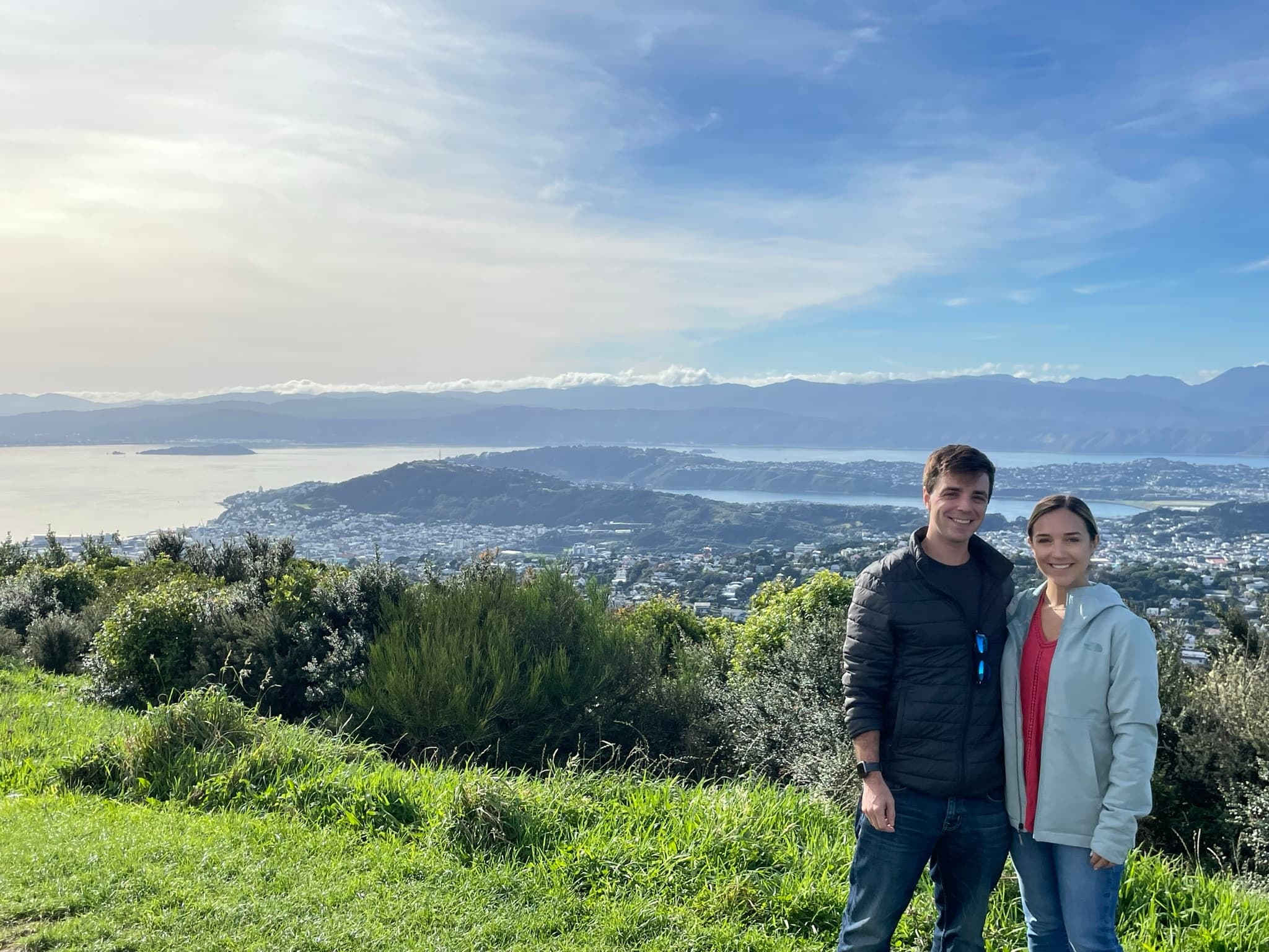 Hikers overlooking city and harbor from green hilltop vista