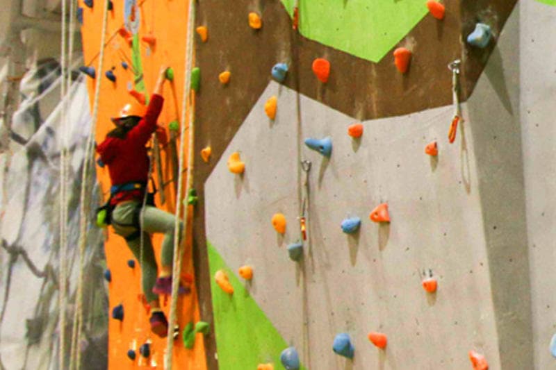 Climber ascending tall indoor lead wall at ArkaPark with colorful holds