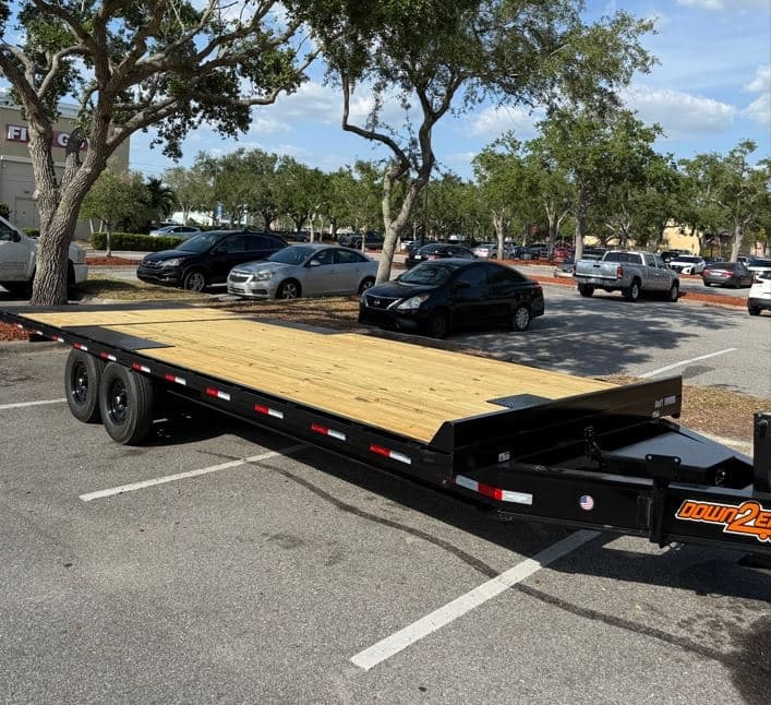 Heavy-duty flatbed trailer parked by tree-lined parking lot
