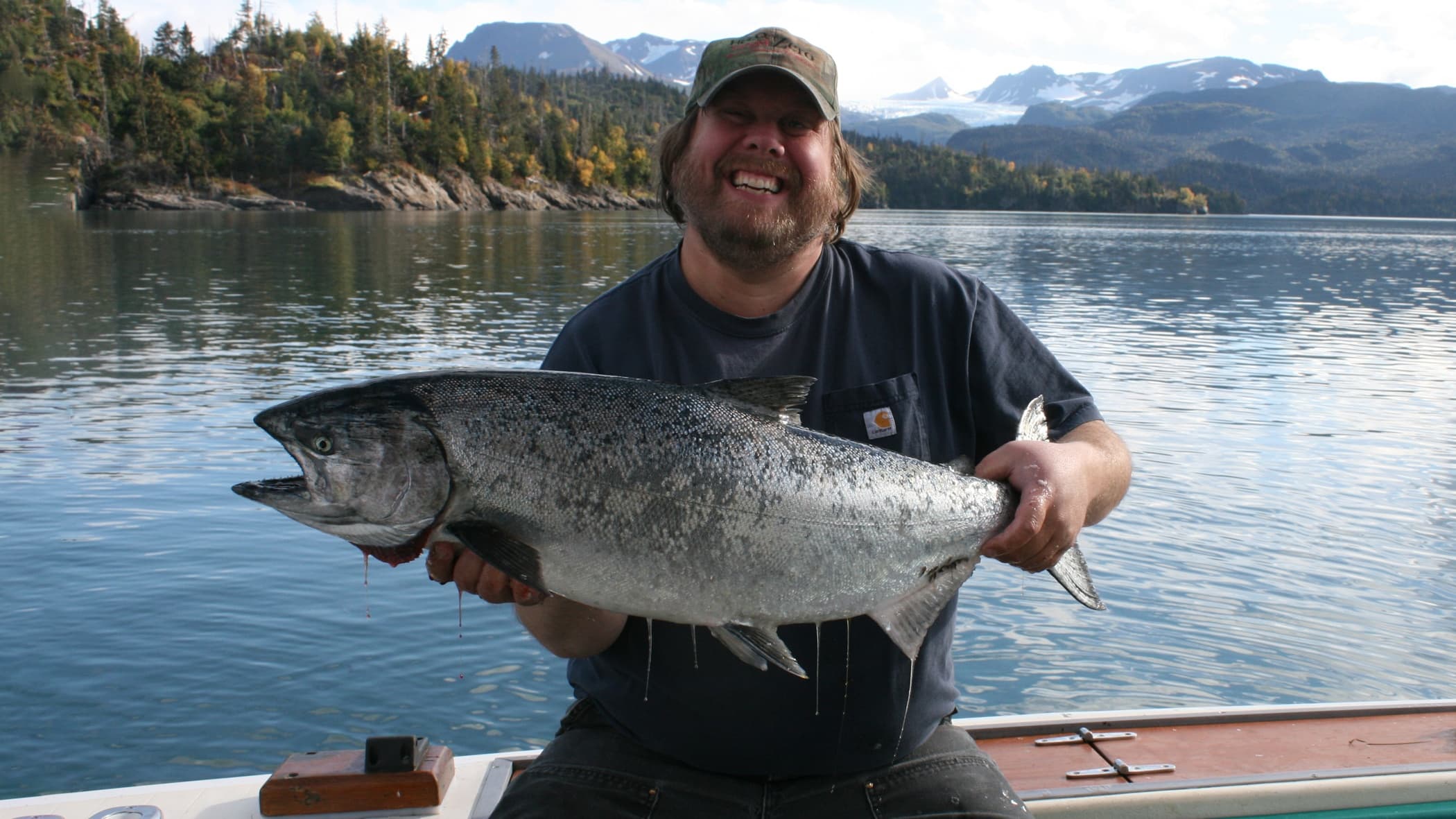 Angler holding large salmon on Alaskan lake with mountains