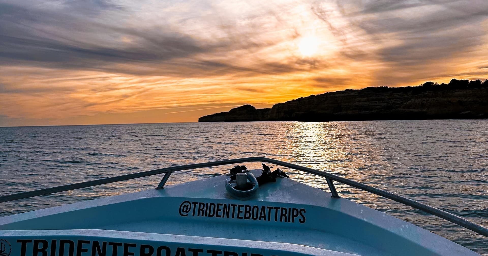 Boat bow heading toward coastal sunset over open ocean