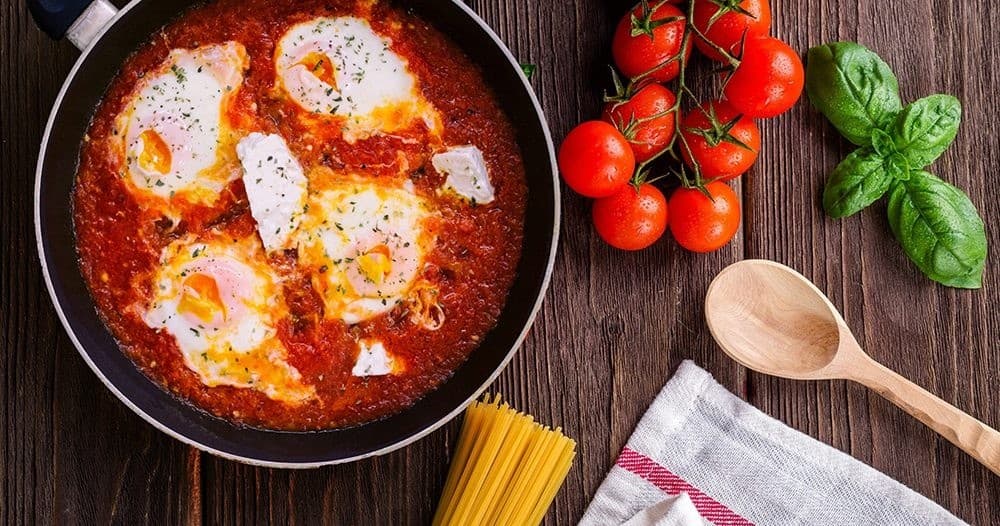 Shakshuka skillet with tomatoes and basil on wooden table, ready to serve