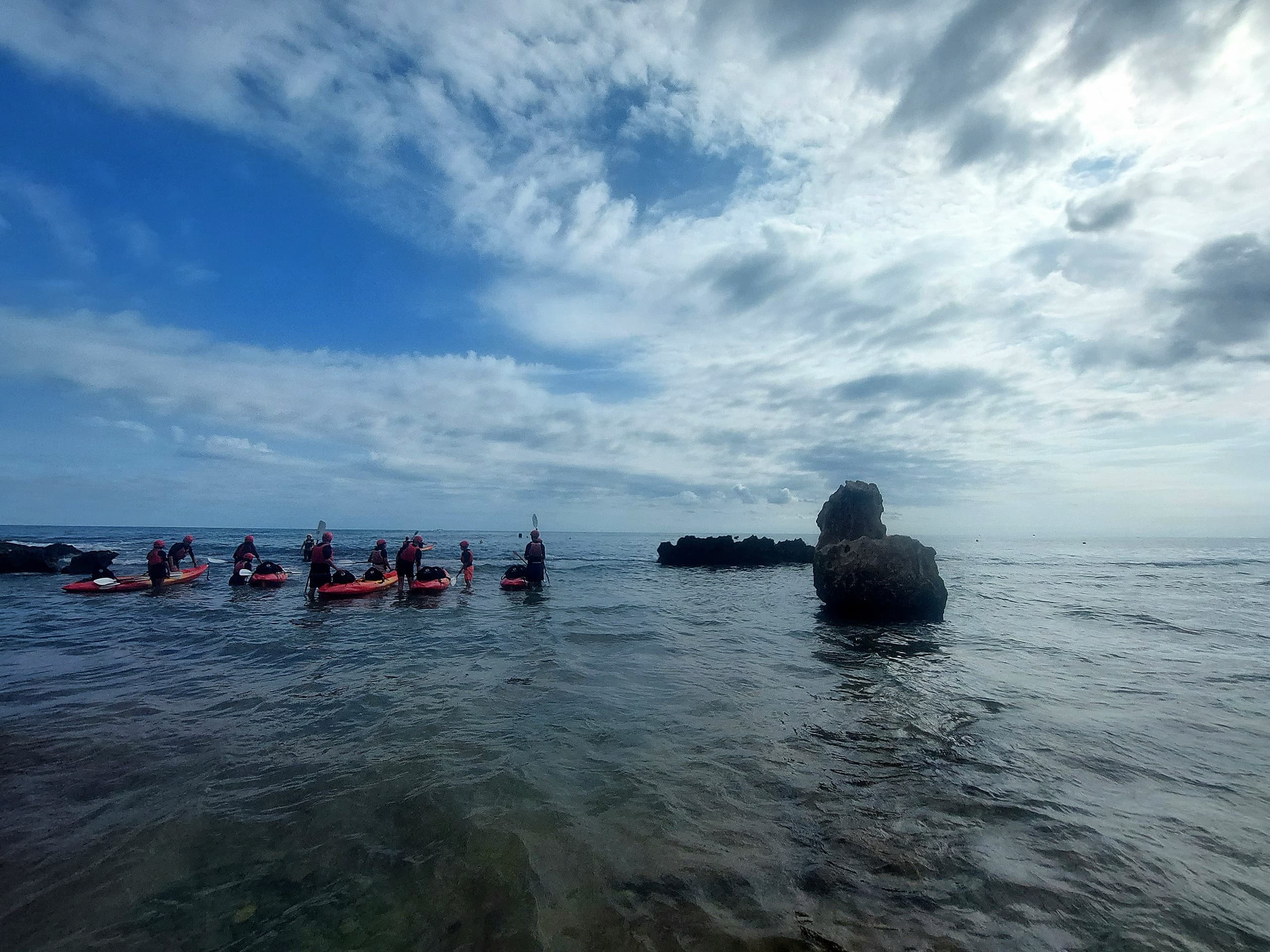 Sea kayakers touring shallow rocky reef under blue sky