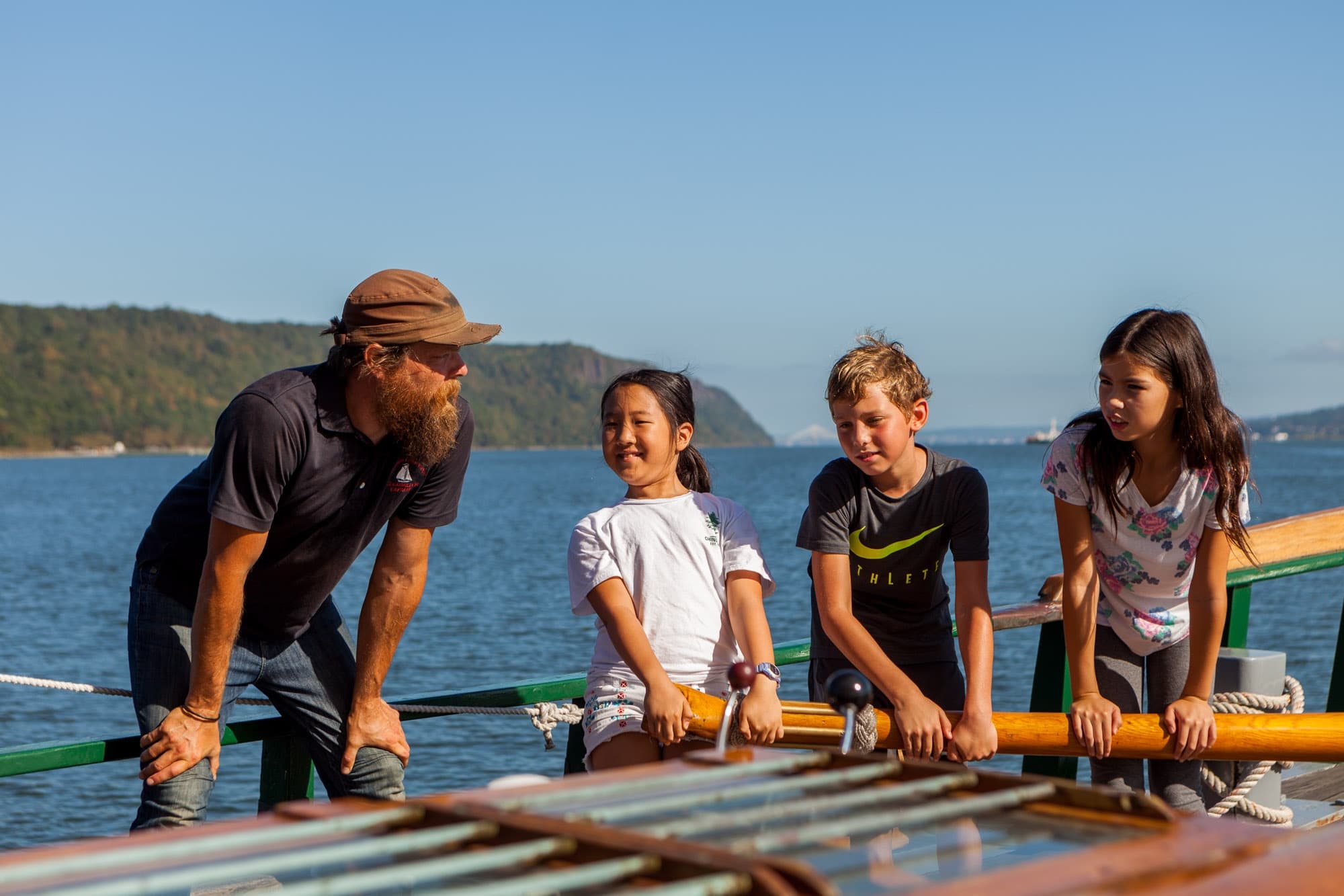 Instructor and kids working on boat deck with coastal hills background