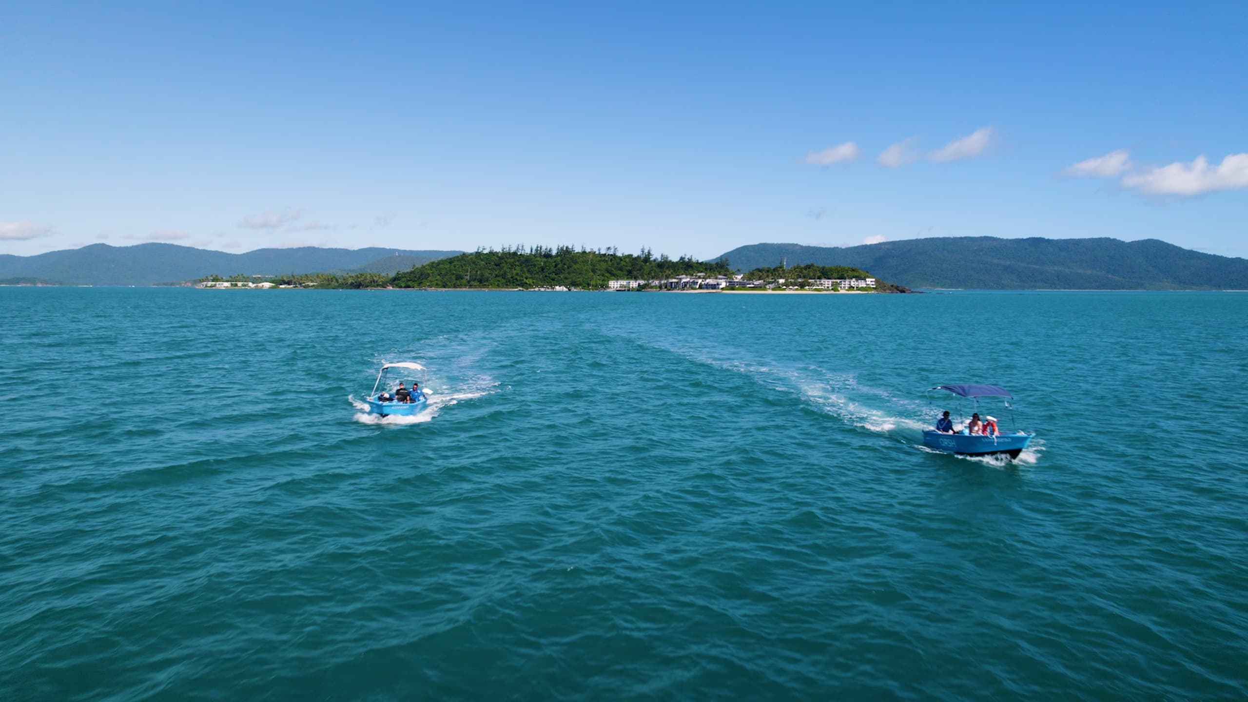 Two boats cruising across wide open ocean with island horizon