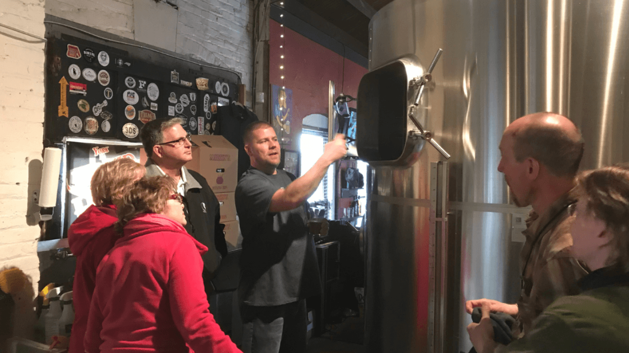 Small group on brewery tour inspecting fermenter tanks in taproom
