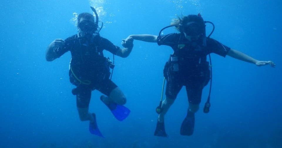 Two scuba divers holding hands in clear blue tropical ocean