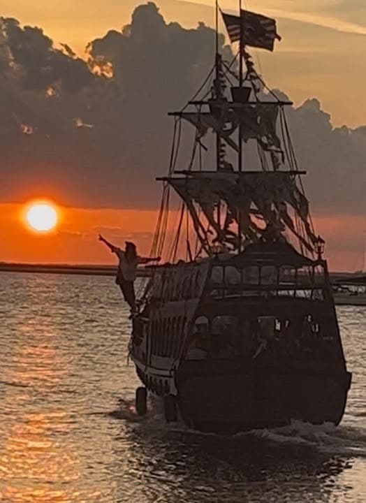 Historic-style pirate ship sailing toward sunset over water