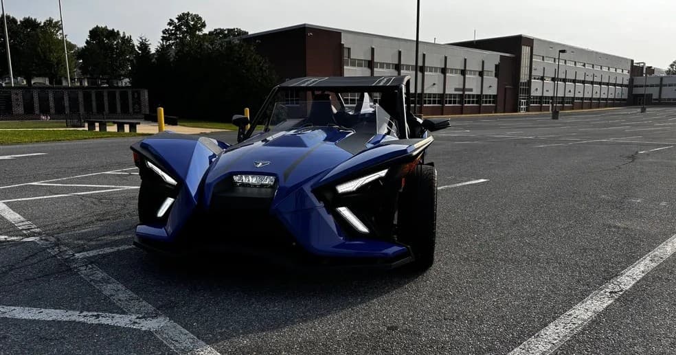 Blue Slingshot parked in urban lot near industrial building