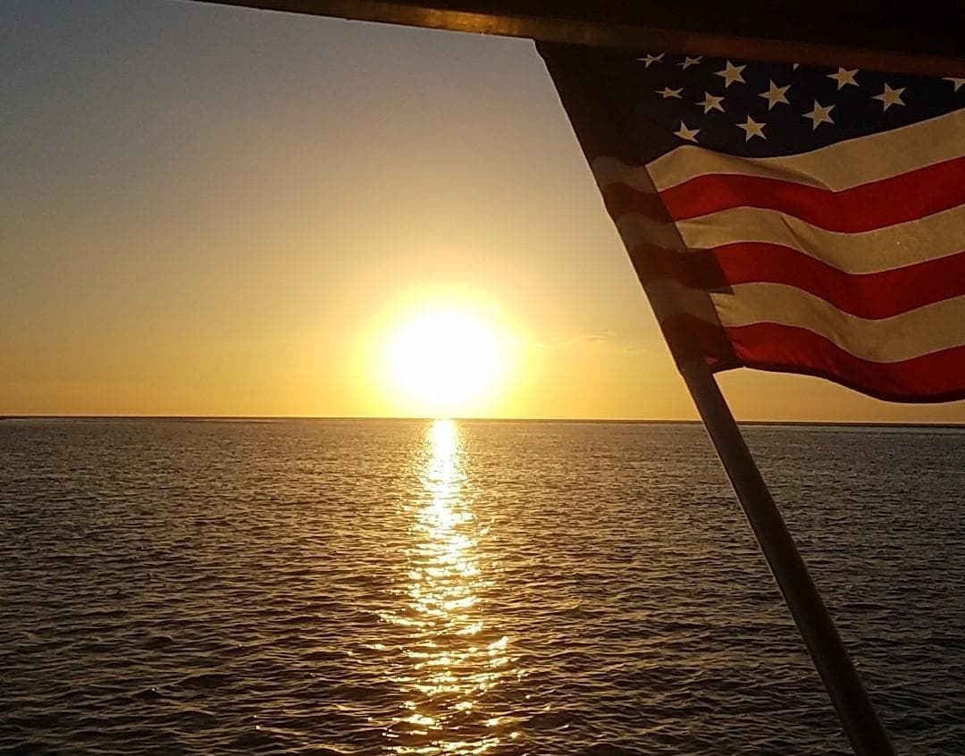 Sunset boat cruise with American flag and ocean horizon view