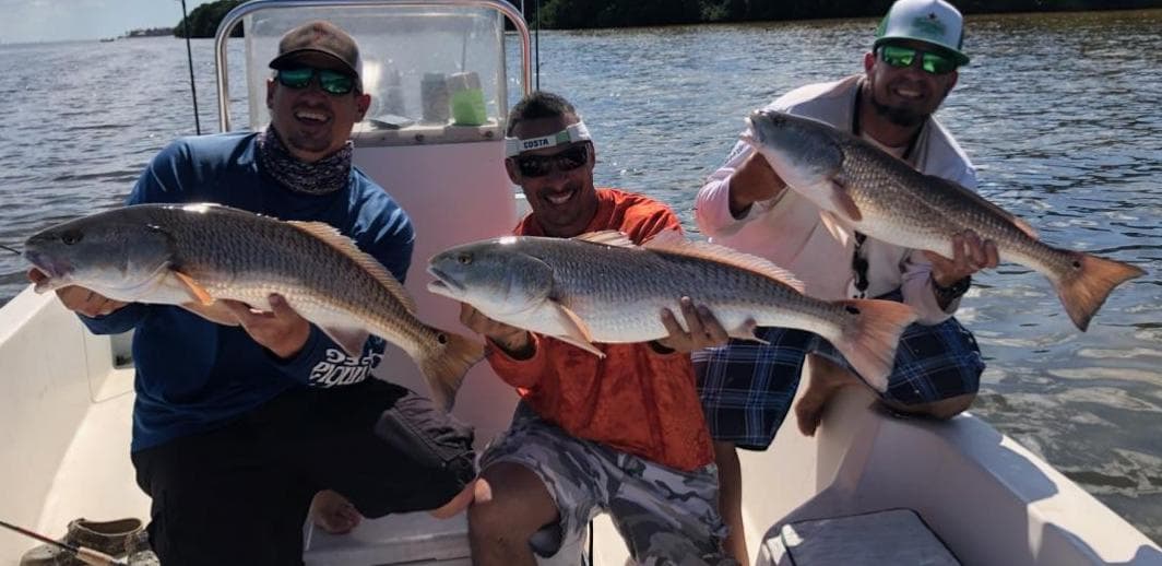 Anglers on boat holding multiple redfish after successful inshore charter