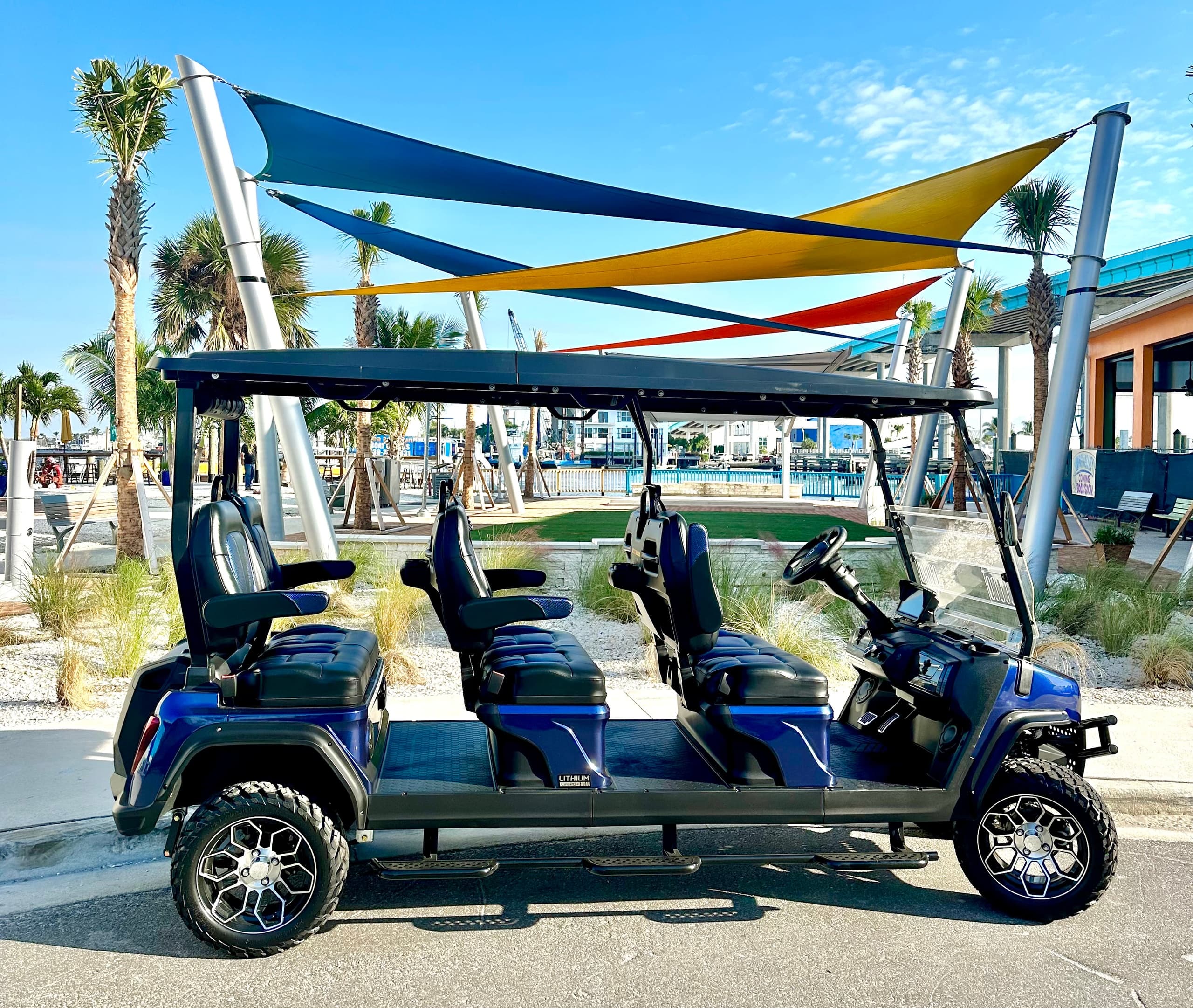Multi-passenger golf cart under shade sails at beachfront