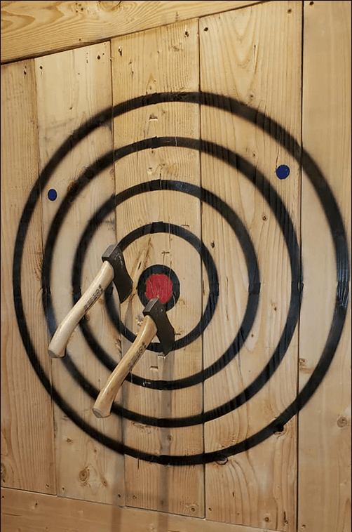 Close-up of axes stuck in wooden target at indoor axe-throwing range